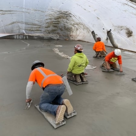 Concrete contractors smoothing concrete slab covered by rain tunnel