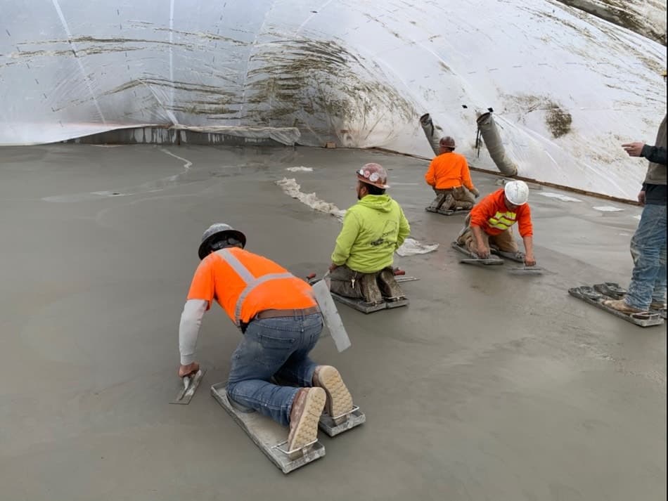 Concrete contractors smoothing concrete slab covered by rain tunnel